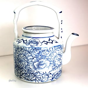 May include: White ceramic teapot with a blue floral pattern. The teapot features a curved handle and spout, and the body is decorated with blue flowers and foliage. A classic piece for tea lovers.