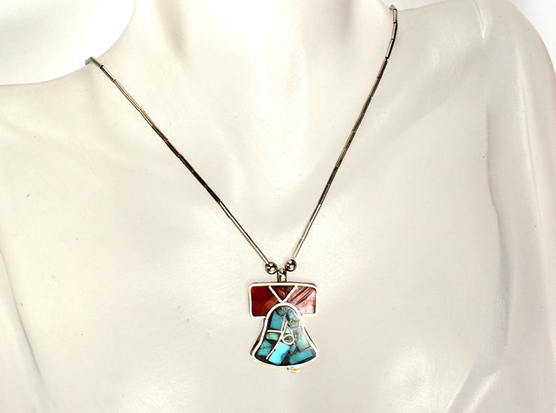 Peut inclure: Un collier en argent avec un pendentif en forme de cloche en turquoise et en pierre rouge.