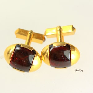 May include: A pair of gold cufflinks with oval-shaped red glass insets.