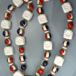 May include: A white, red, and blue beaded necklace with a floral design. The necklace is made of plastic beads and has a metal clasp.