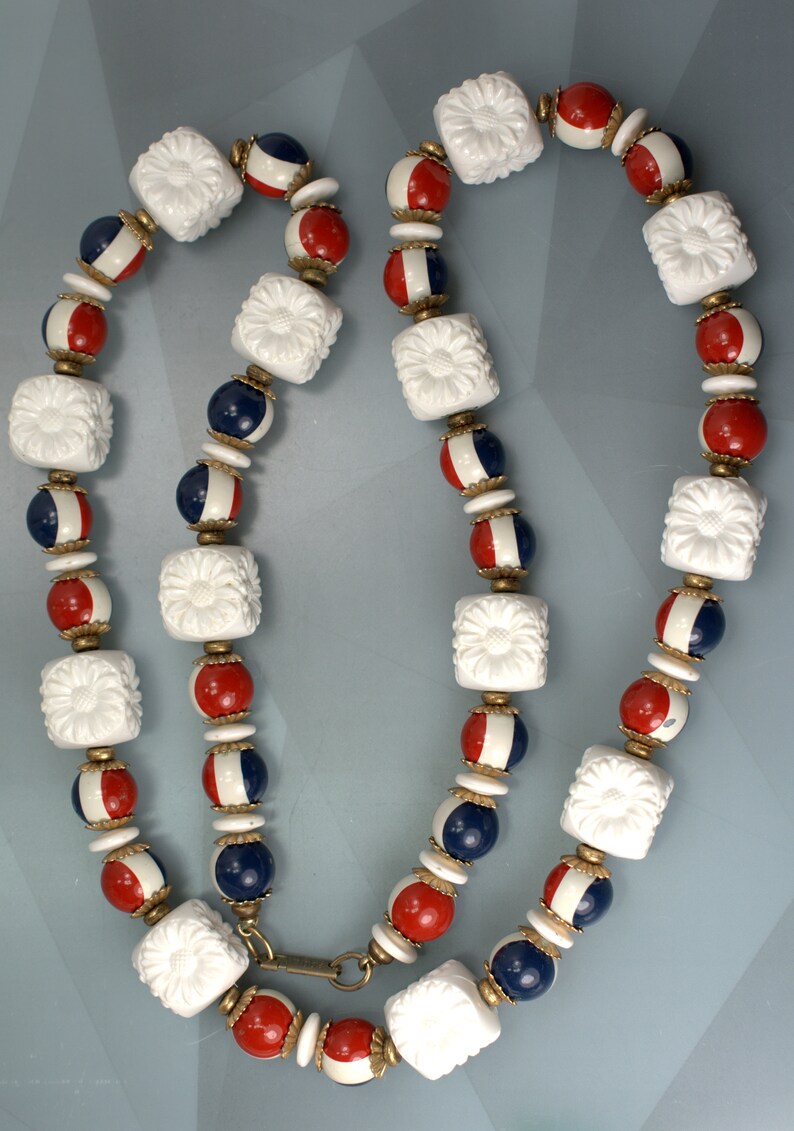 May include: A white, red, and blue beaded necklace with a floral design. The necklace is made of plastic beads and has a metal clasp.