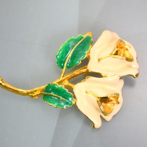 May include: A gold-tone brooch with two white enamel roses and green enamel leaves.