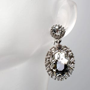 May include: Silver dangle earrings with a large clear crystal surrounded by smaller crystals.
