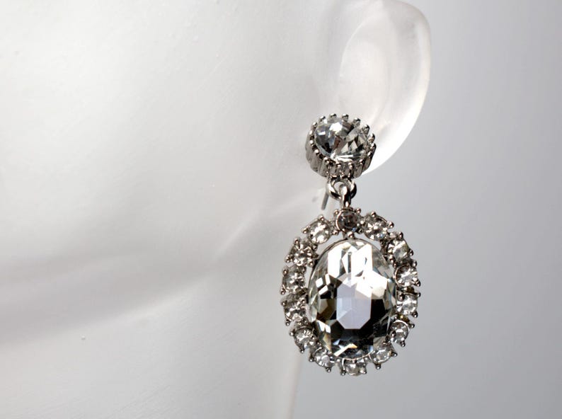 May include: Silver dangle earrings with a large clear crystal surrounded by smaller crystals.