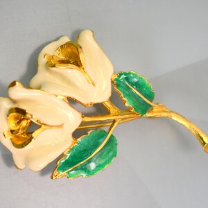 May include: A gold-tone brooch featuring two white enamel roses with green enamel leaves.
