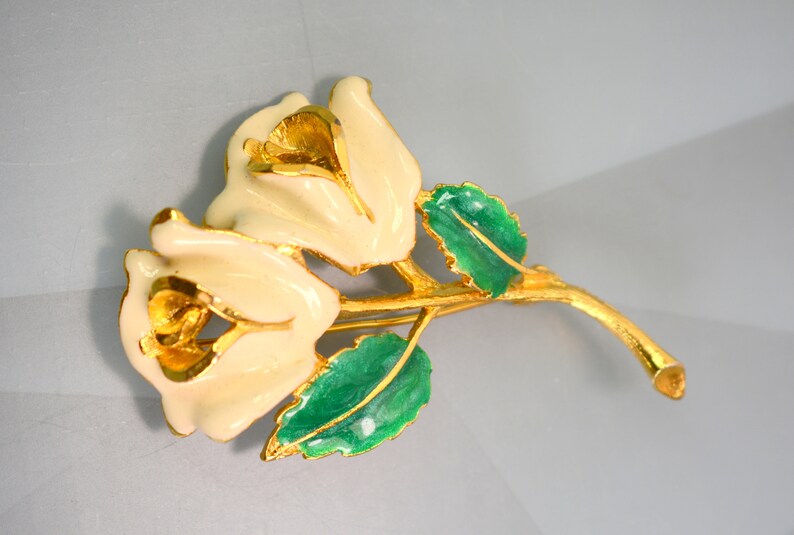 May include: A gold-tone brooch featuring two white enamel roses with green enamel leaves.
