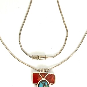 Peut inclure: Un collier en cha&icirc;ne argent avec un pendentif en forme de cloche. Le pendentif est fait de turquoise et de pierres rouges.