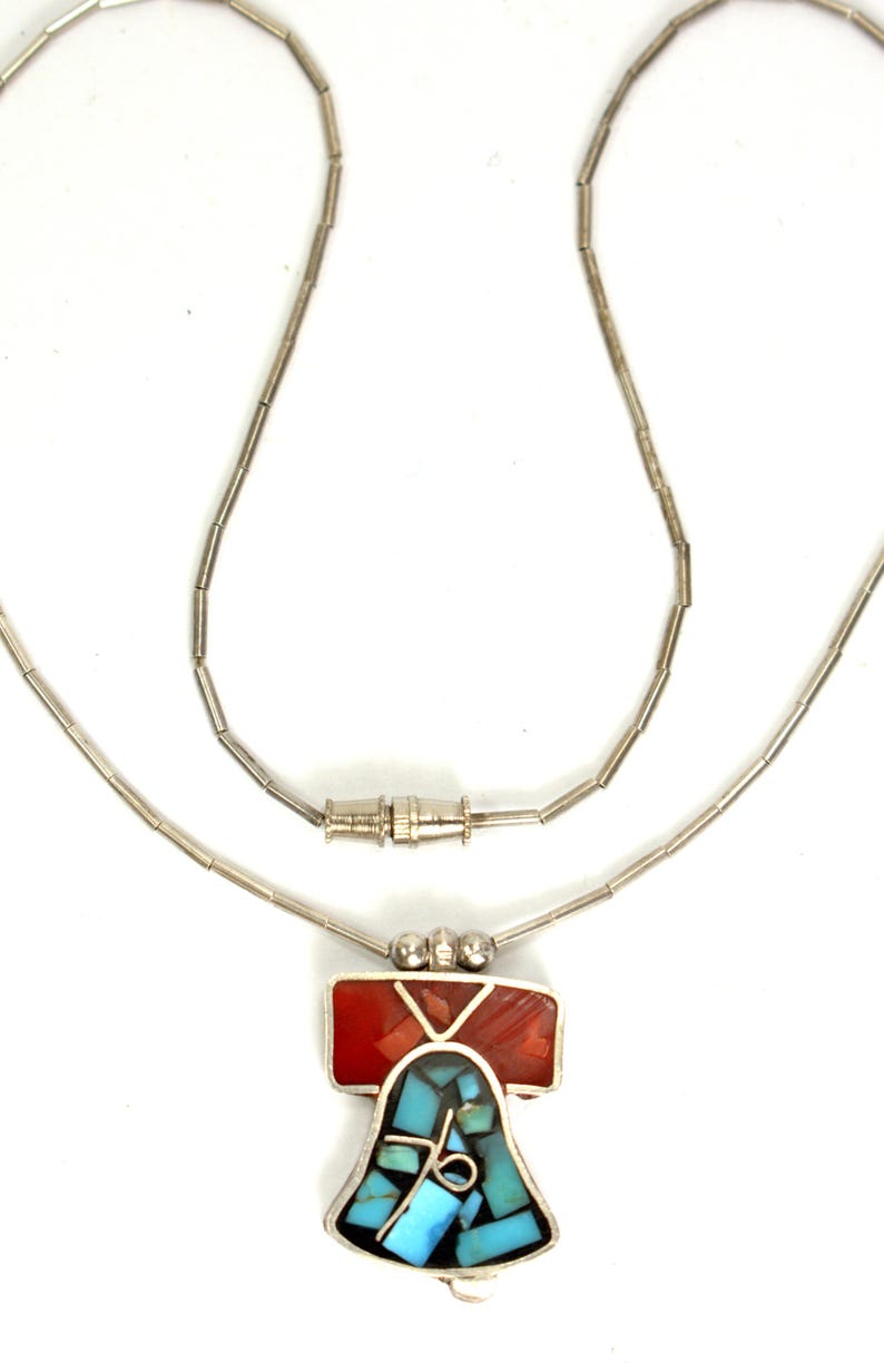 Peut inclure: Un collier en cha&icirc;ne argent avec un pendentif en forme de cloche. Le pendentif est fait de turquoise et de pierres rouges.