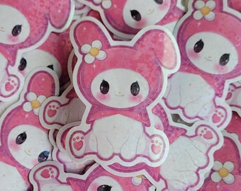 May include: A stack of pink and white stickers featuring a cartoon bunny with a pink bow and a flower on its head. The stickers have a sparkly, iridescent finish.