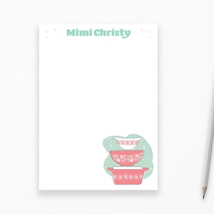 May include: A white notepad with the text "Mimi Christy" at the top. The notepad has a green background with a stack of three pink and white bowls with floral designs.
