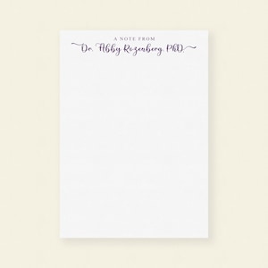 May include: A white notepad with a purple inscription that reads "A Note From Dr. Abby Rosenberg, PhD."