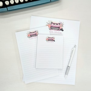 May include: Three lined notepads with a pink typewriter and floral design. The notepads have the name "Faith Olsson" printed on them.