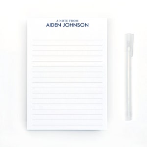 May include: A white notepad with blue lined paper and the text "A Note From Aiden Johnson" at the top. A clear pen is lying next to the notepad.