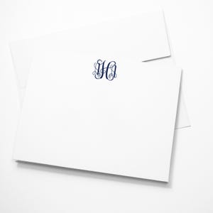 May include: A white stationery card and matching envelope featuring a dark blue monogram with the letters J, H, and A in an interlocking script font centered at the top of the card. The card is rectangular with a clean, smooth surface.