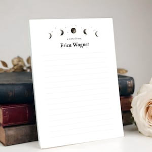 May include: A white notepad with lined pages. The top of the notepad features a black graphic of the phases of the moon and the text "a note from Erica Wagner."