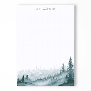 May include: A white notepad with the name "ART WAGNER" printed at the top. The bottom of the notepad features a watercolor illustration of a forest with green trees and a misty background.