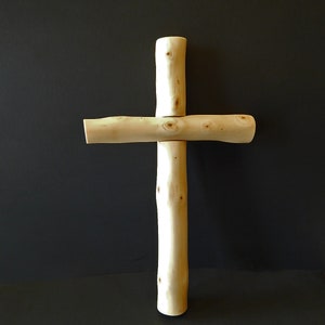 Puede incluir: Una cruz de madera hecha de ramas naturales. La cruz es de color marr&oacute;n claro y tiene un aspecto r&uacute;stico y artesanal.
