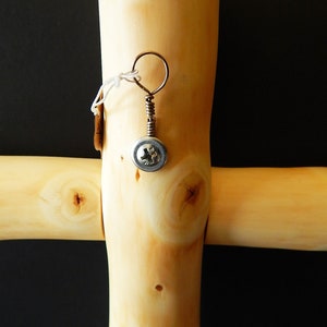 Puede incluir: Una cruz de madera con un peque&ntilde;o tornillo de metal sujeto a ella. El tornillo tiene un alambre de cobre envuelto alrededor y un peque&ntilde;o anillo de metal en la parte superior.