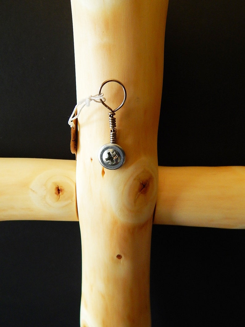 Puede incluir: Una cruz de madera con un peque&ntilde;o tornillo de metal sujeto a ella. El tornillo tiene un alambre de cobre envuelto alrededor y un peque&ntilde;o anillo de metal en la parte superior.