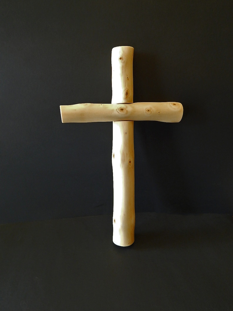 Puede incluir: Una cruz de madera hecha de ramas naturales. La cruz es de color marr&oacute;n claro y tiene un aspecto r&uacute;stico y artesanal.