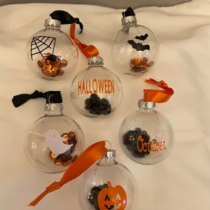 May include: Five clear glass ornaments with orange and black Halloween-themed decorations. The ornaments feature a spider web, bats, a ghost, a pumpkin, and the word "October".