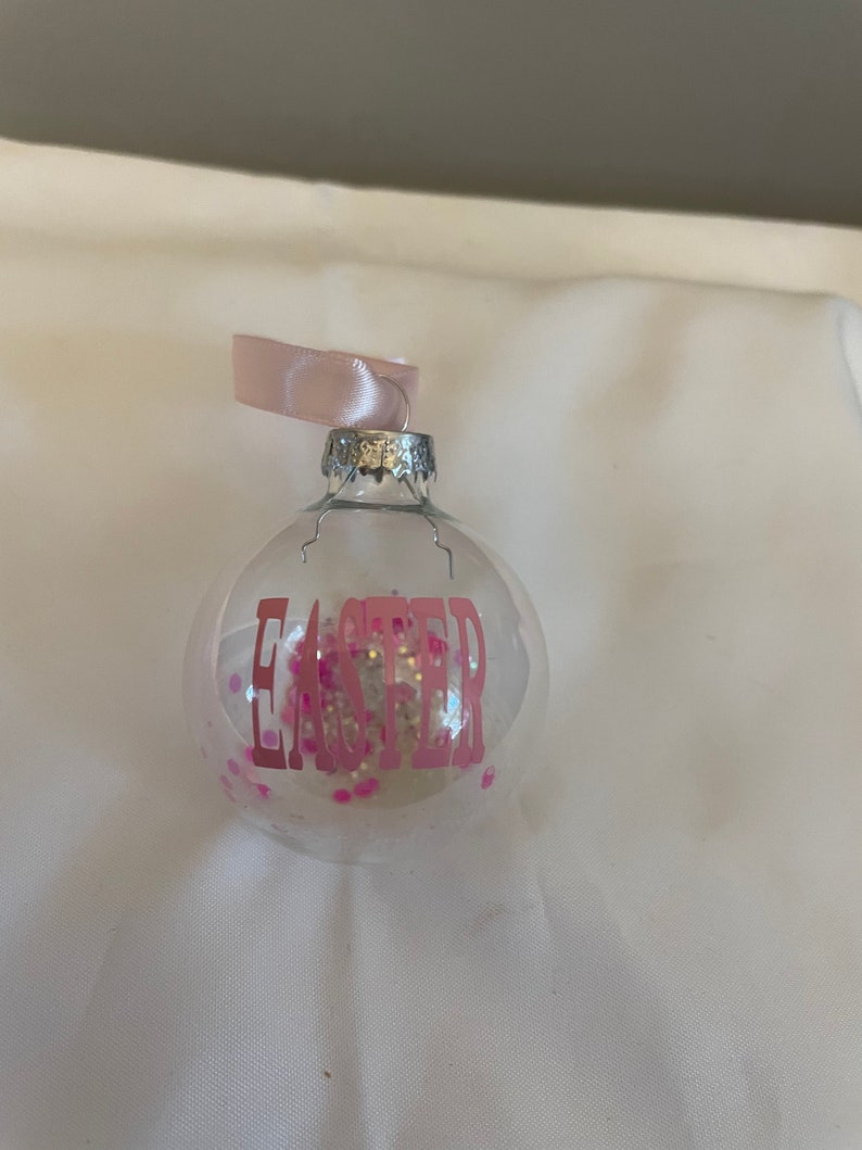 May include: A clear glass ornament with pink glitter and the word "Easter" in pink lettering.