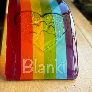 Puede incluir: Un memorial para mascotas de vidrio rectangular con un dise&ntilde;o de arco&iacute;ris. El vidrio presenta un coraz&oacute;n con una huella de pata y el nombre "Blanki" grabado en blanco. Los colores incluyen rojo, naranja, amarillo, verde, azul y morado.