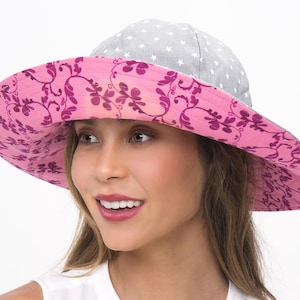 Puede incluir: Un sombrero de sol de ala ancha con un estampado floral rosa en la parte inferior del ala y una tela gris con estrellas blancas en la parte superior. El sombrero lo lleva una persona con el pelo largo y casta&ntilde;o.