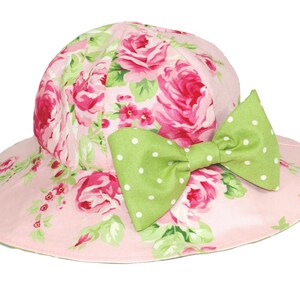 Puede incluir: Un sombrero de sol rosa con estampado floral y un lazo verde con lunares.