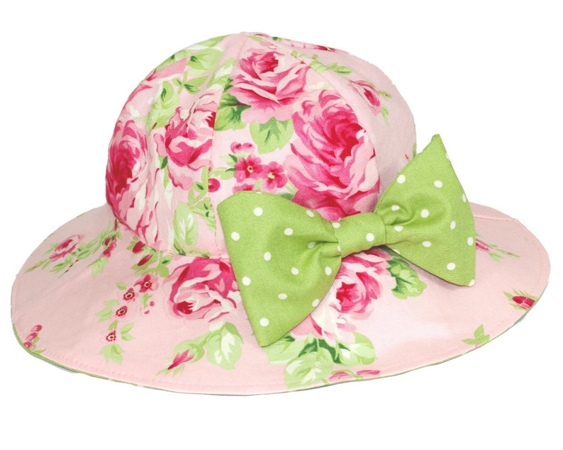 Puede incluir: Un sombrero de sol rosa con estampado floral y un lazo verde con lunares.