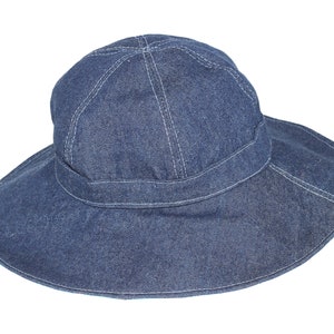 Puede incluir: Un sombrero de sol de denim de ala ancha de color azul oscuro. El sombrero tiene una banda cosida alrededor de la corona y un ala ancha.