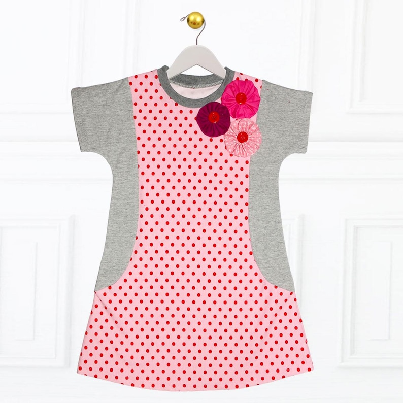 May include: A pink and gray polka dot dress with short sleeves and a flower embellishment on the front.