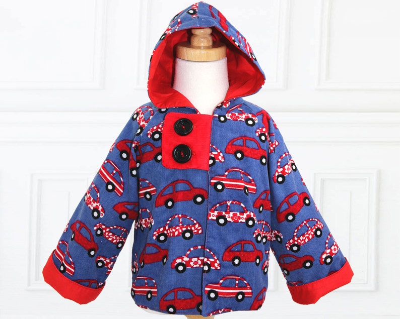 May include: A blue hooded jacket with red trim and a red car print. The jacket has two black buttons.