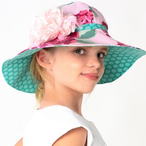 Puede incluir: Un sombrero de sol floral rosa y verde con una gran flor rosa en el lateral. El sombrero tiene un forro de lunares.