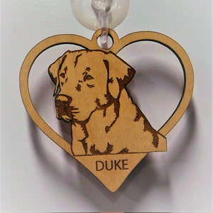 May include: Wooden heart-shaped ornament with a laser-engraved image of a brown Labrador Retriever. The dog's name, "DUKE", is engraved below the image.