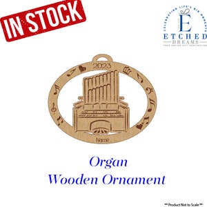 May include: A wooden ornament shaped like an organ with musical notes around the edge. The ornament is brown and has the year 2023 and the word "Name" on it.  Organ Wooden Ornament.
