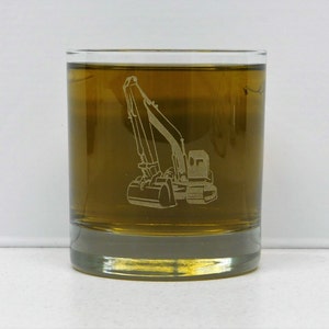 May include: A clear glass tumbler with an etched design of an excavator. The tumbler is filled with a light brown liquid.