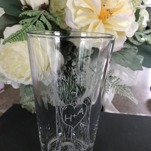 May include: A clear glass with a design of two trees with a heart in the middle. The heart has the initials "H+A" inside.