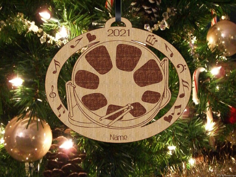 May include: A wooden Christmas ornament shaped like a steel drum with musical notes and a heart around the edge. The ornament is brown and has the year 2021 and the word "Name" on it.