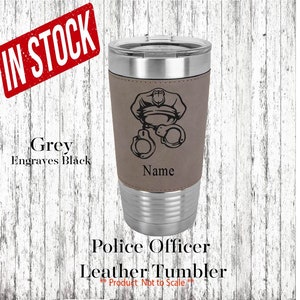 May include: A stainless steel tumbler with a brown leather wrap. The wrap features a black silhouette of a police officer's hat and handcuffs. The text "Name" is engraved on the wrap.  Grey engraves black.