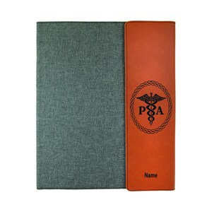 May include: A brown leatherette folder with a gray fabric cover. The folder has a pocket on the right side with a medical symbol and the letters "PA" engraved on it. The text "Name" is also engraved on the pocket.