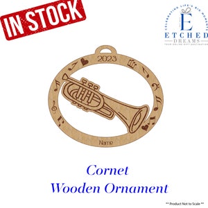 May include: A wooden cornet ornament with a circular frame featuring musical notes and a heart. The year 2023 is engraved at the top. The word "Name" is below the cornet. The words "Cornet Wooden Ornament" are at the bottom.