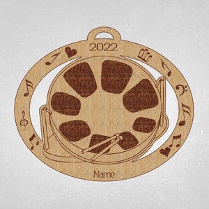 May include: A brown wooden ornament shaped like a steel drum with musical notes and a heart around the edge. The ornament has the year 2022 and the word "Name" inscribed on it.