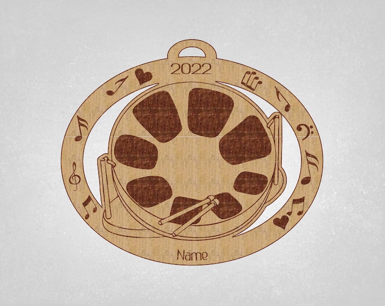 May include: A brown wooden ornament shaped like a steel drum with musical notes and a heart around the edge. The ornament has the year 2022 and the word "Name" inscribed on it.