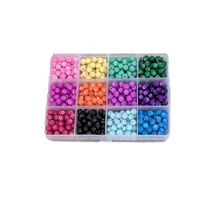 May include: A clear plastic organizer filled with colorful beads. The beads are in various colors, including pink, yellow, teal, green, purple, orange, black, light blue, and dark blue. The beads are round and appear to be made of plastic.
