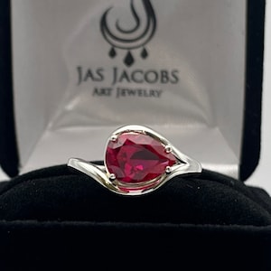 May include: A white ceramic mug with a black handle and the text "But First, Coffee" in a bold, black font. The mug is set against a blurred background, suggesting a cozy setting.