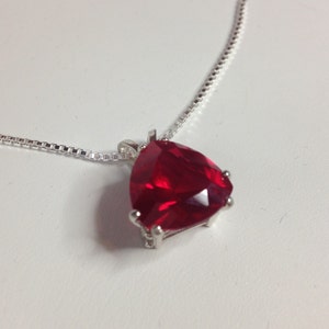 May include: A silver chain necklace with a large, red, heart-shaped gemstone pendant.