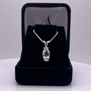 May include: A silver chain necklace with a marquise-shaped clear gemstone pendant in a black velvet box.