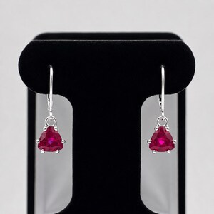 May include: A pair of silver leverback earrings featuring faceted, triangular-cut deep red stones. Each stone is secured by three small silver prongs, suspended from a polished silver hook mechanism that provides a secure closure for the wearer.