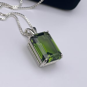 May include: A silver chain necklace with a green gemstone pendant. The gemstone is cut in an emerald shape and has a faceted finish.
